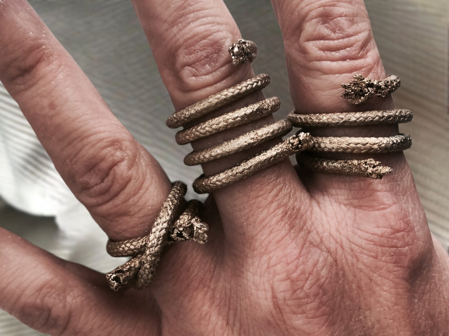 A hand adorned with multiple Curly Handcrafted Rope Ring III pieces on the fingers, each meticulously handmade and elegantly gold plated—a true testament to the craftsmanship of Angela Lago.