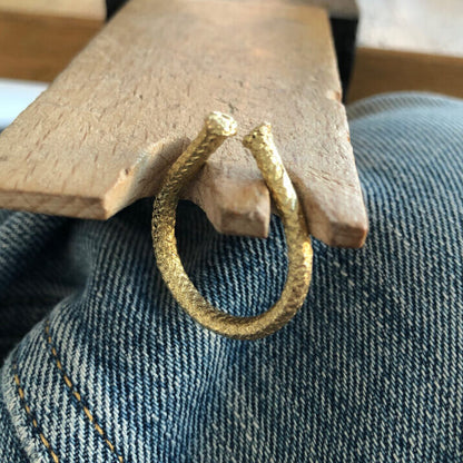 A 24k gold-plated Golden Open Rope Ring with a textured surface lies on a denim fabric, positioned against a wooden surface.