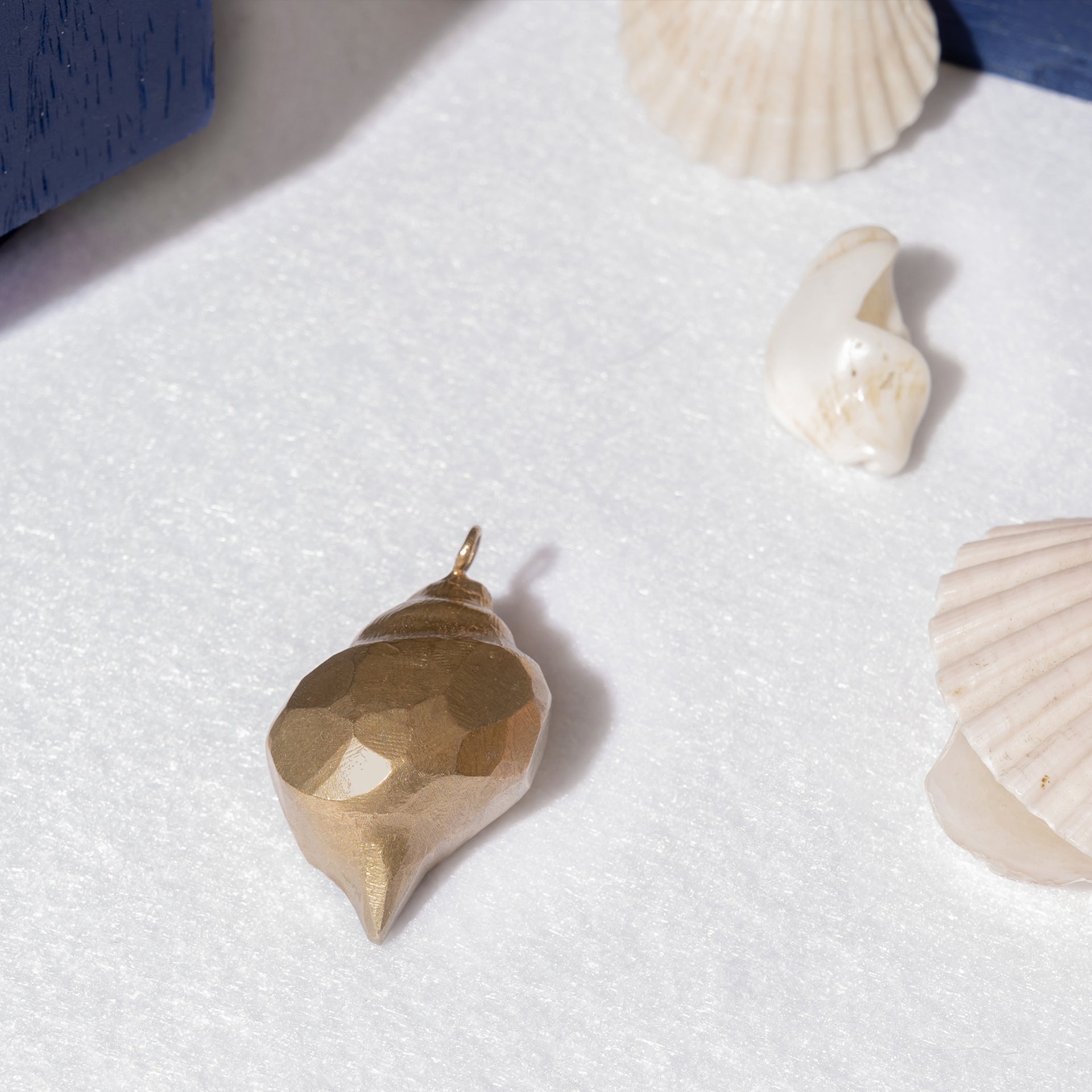 A unique piece, the Nautical Handcrafted Seashell One of A Kind Pendant Nº 1 in gold color lies on a white surface among three real seashells. Handmade by Angela Lago, it sparkles with the elegance of a black diamond.