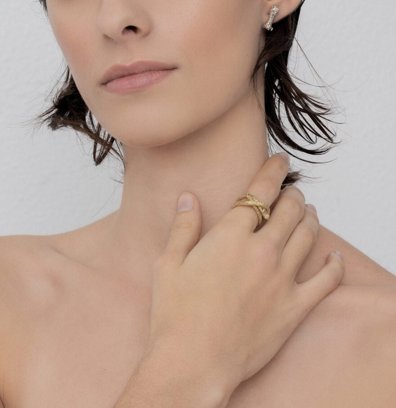 A person wearing a Ballestrinque Knot - Clove hitch Artisanal Nautical Ring on their finger and a sterling silver diamond earring, touching their neck with a neutral expression.