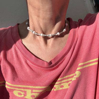 A person wearing a pink shirt with yellow stripes and a Sterling ropes and freshwater pearls choker handmade by Angela Lago. The image focuses on the neck and upper chest area.