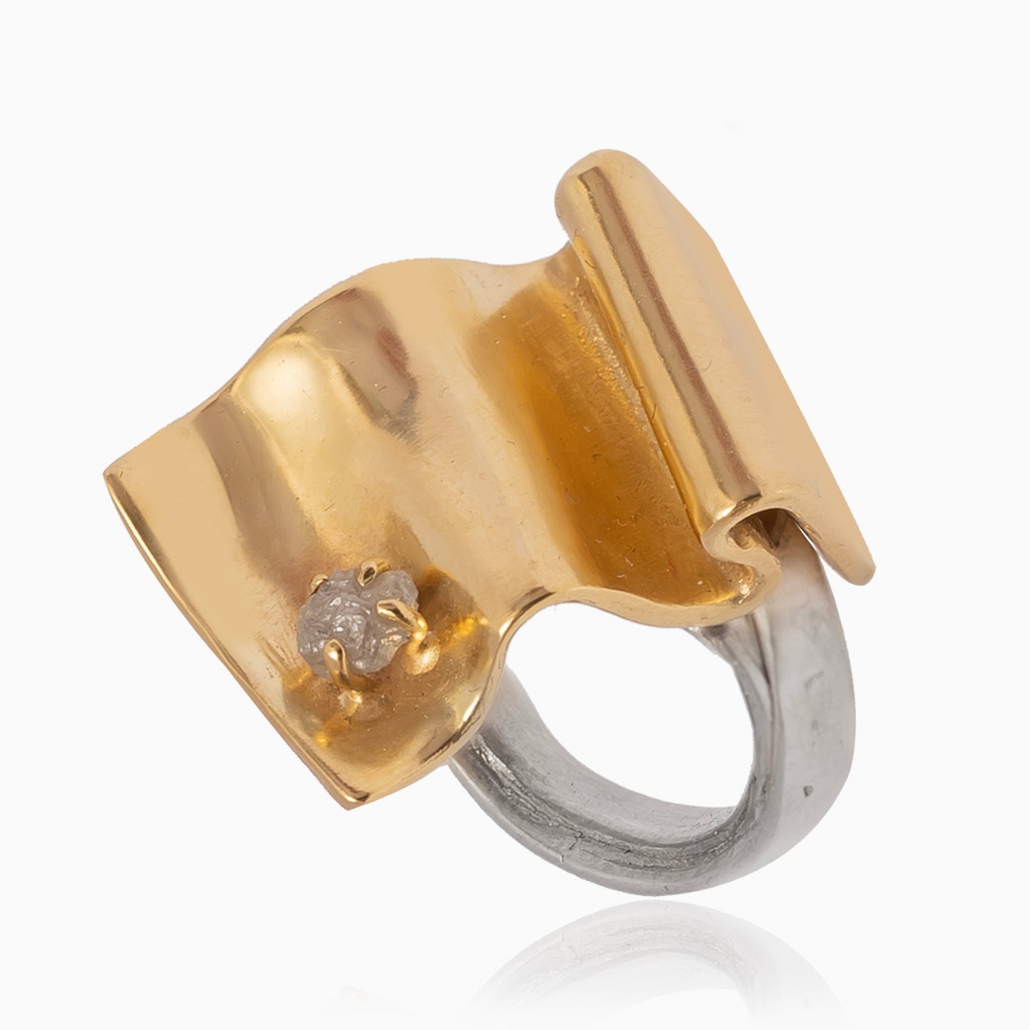 The Golden Handcraft Ring Wave with Raw Diamond is a sterling silver and gold plated brass piece featuring an abstract, folded design with a small, embedded raw diamond.