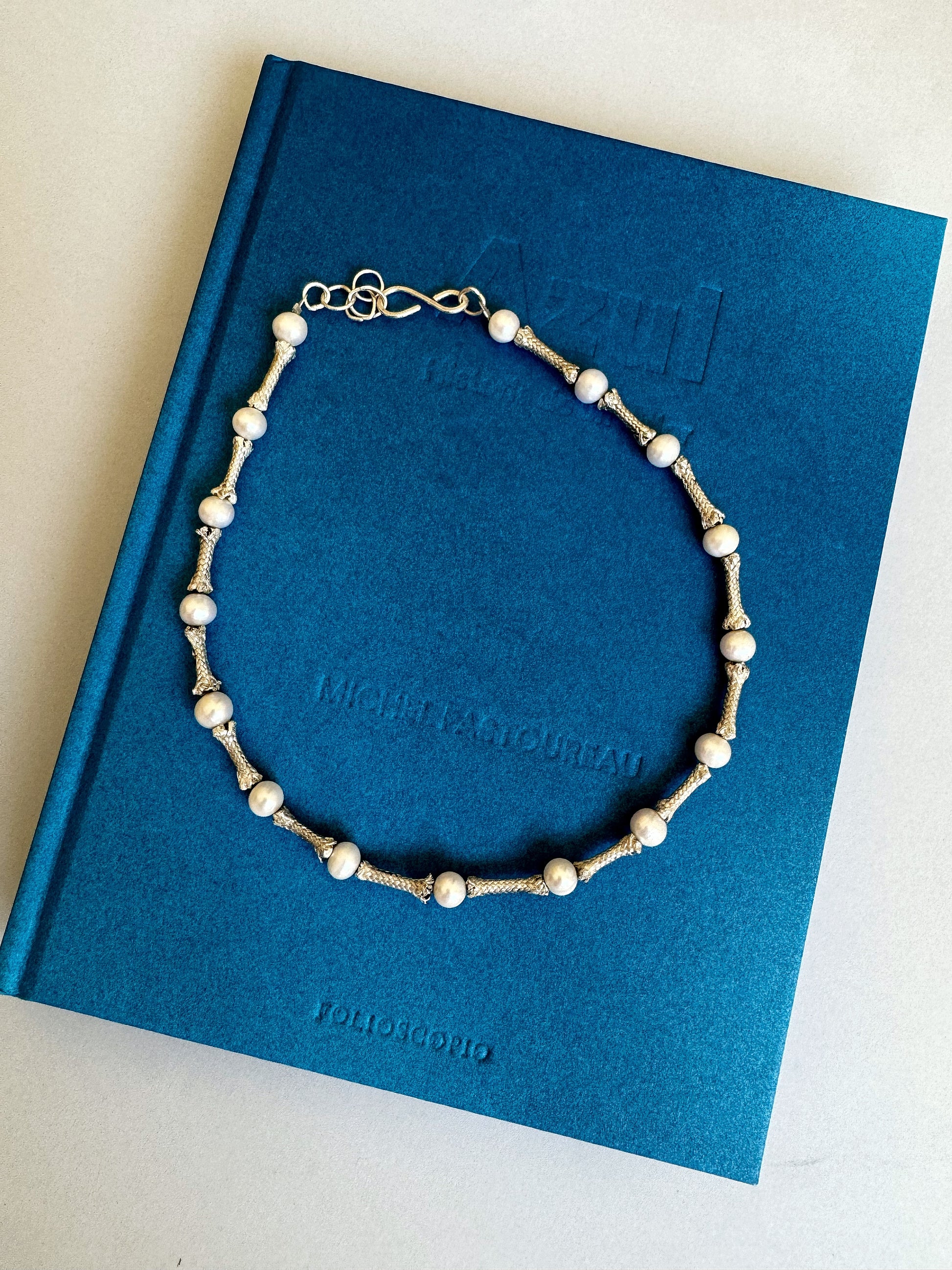 A Sterling ropes and freshwater pearls choker, handmade by Angela Lago, is laid on top of a blue book titled "Azul" by Miguel Arturo.