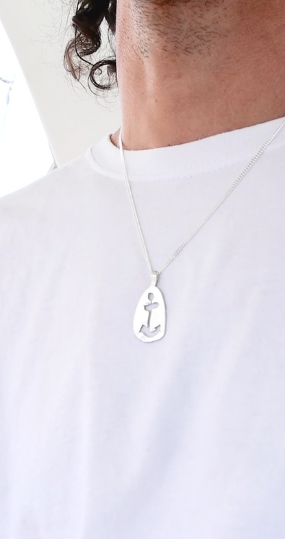 A person wearing a white t-shirt is shown with the Anchor Sketch Pendant Inspired by Bernard Moitessier’s Spirit, showcasing an elegant piece of maritime jewelry.