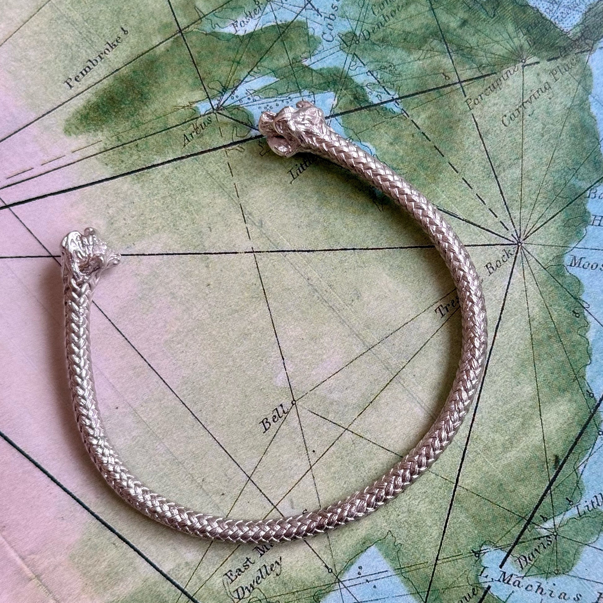 A Sterling Silver Thick Rope Cuff Bracelet with lion head ends, handmade in Madrid, is elegantly placed on an old nautical map.