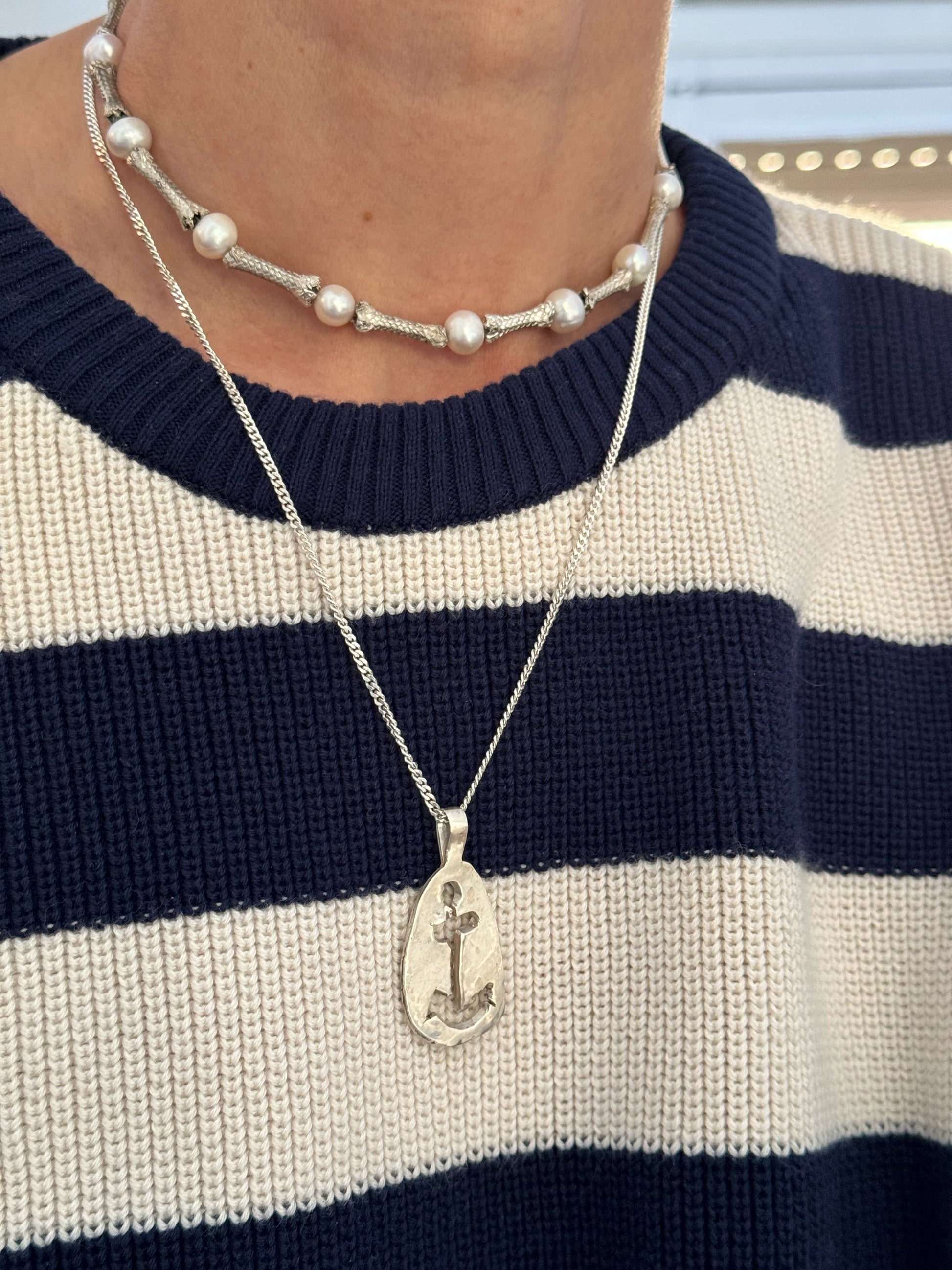 Close-up of a person wearing a striped navy and white sweater, a pearl choker, and maritime jewelry featuring the "Anchor Sketch Pendant Inspired by Bernard Moitessier’s Spirit" in sterling silver.