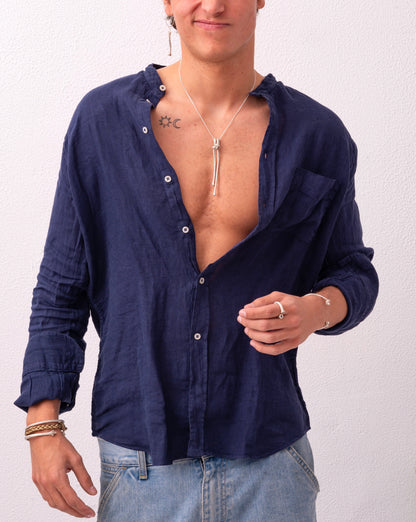 A person is wearing a partially unbuttoned blue shirt with rolled-up sleeves, paired with jeans and an Artisanal Made Ballestrinque Nautical Knot Pendant. Tattoos are visible on their chest.