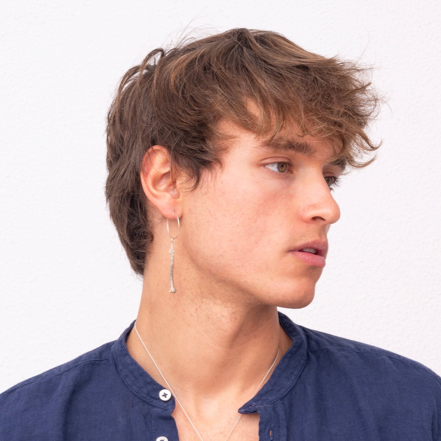 A young person with short brown hair, wearing a blue button-up shirt and a Thin Hoop Nautical Earring with Sterling Silver Rope, looking to the side.