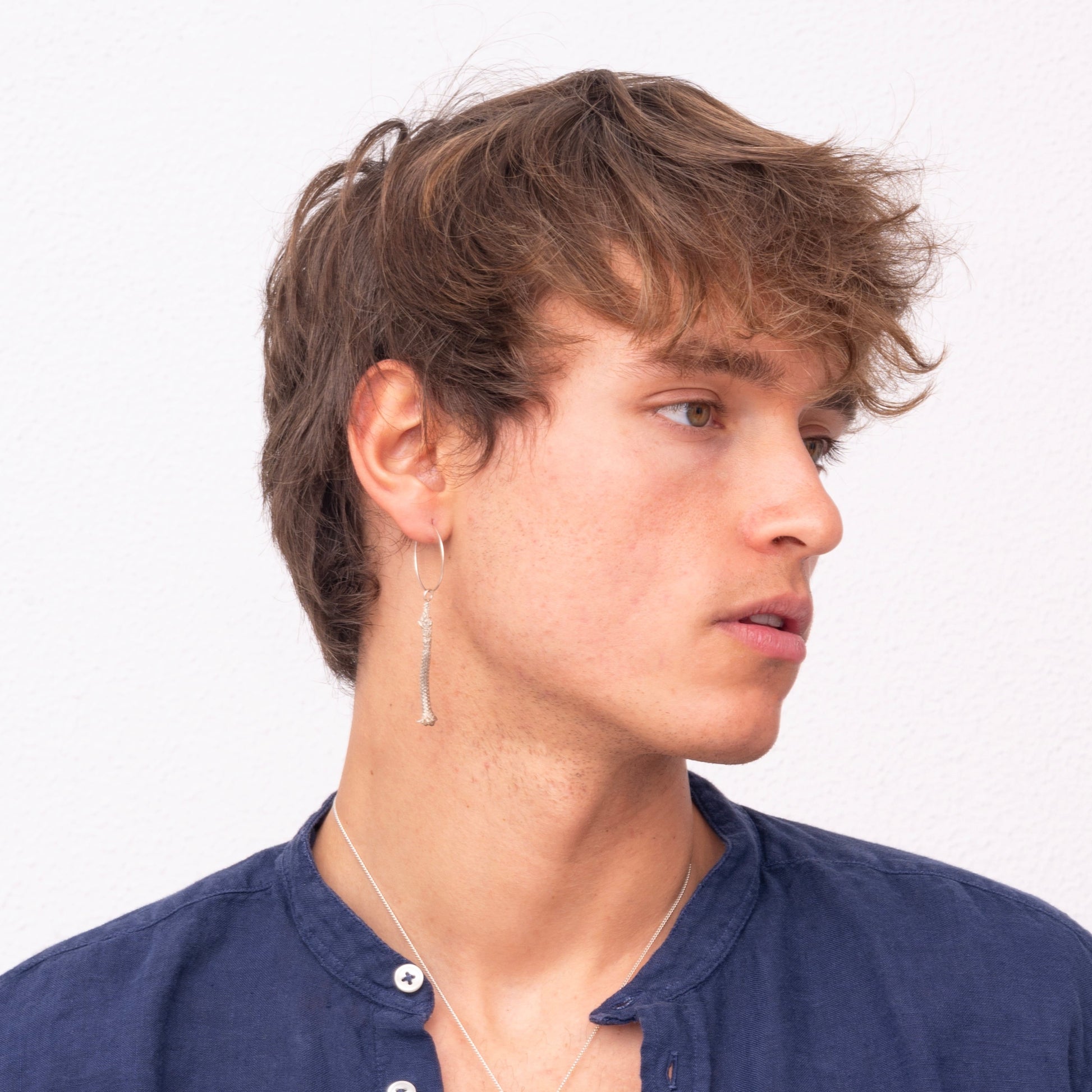 A young person with short brown hair, wearing a blue button-up shirt and a Thin Hoop Nautical Earring with Sterling Silver Rope, looking to the side.