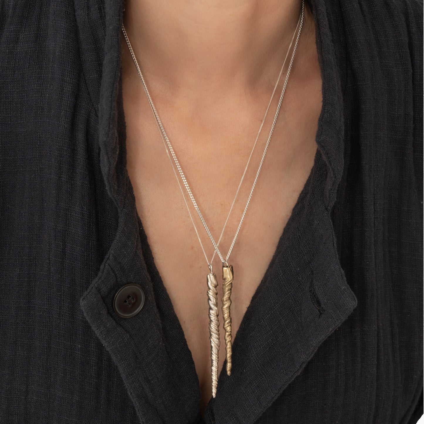 Close-up of a person wearing a dark jacket, featuring two long, pendant necklaces with twisted designs. One is the Narwhal Tusk Handmade Tooth Pendant adorned with sterling silver, handmade by Angela Lago.