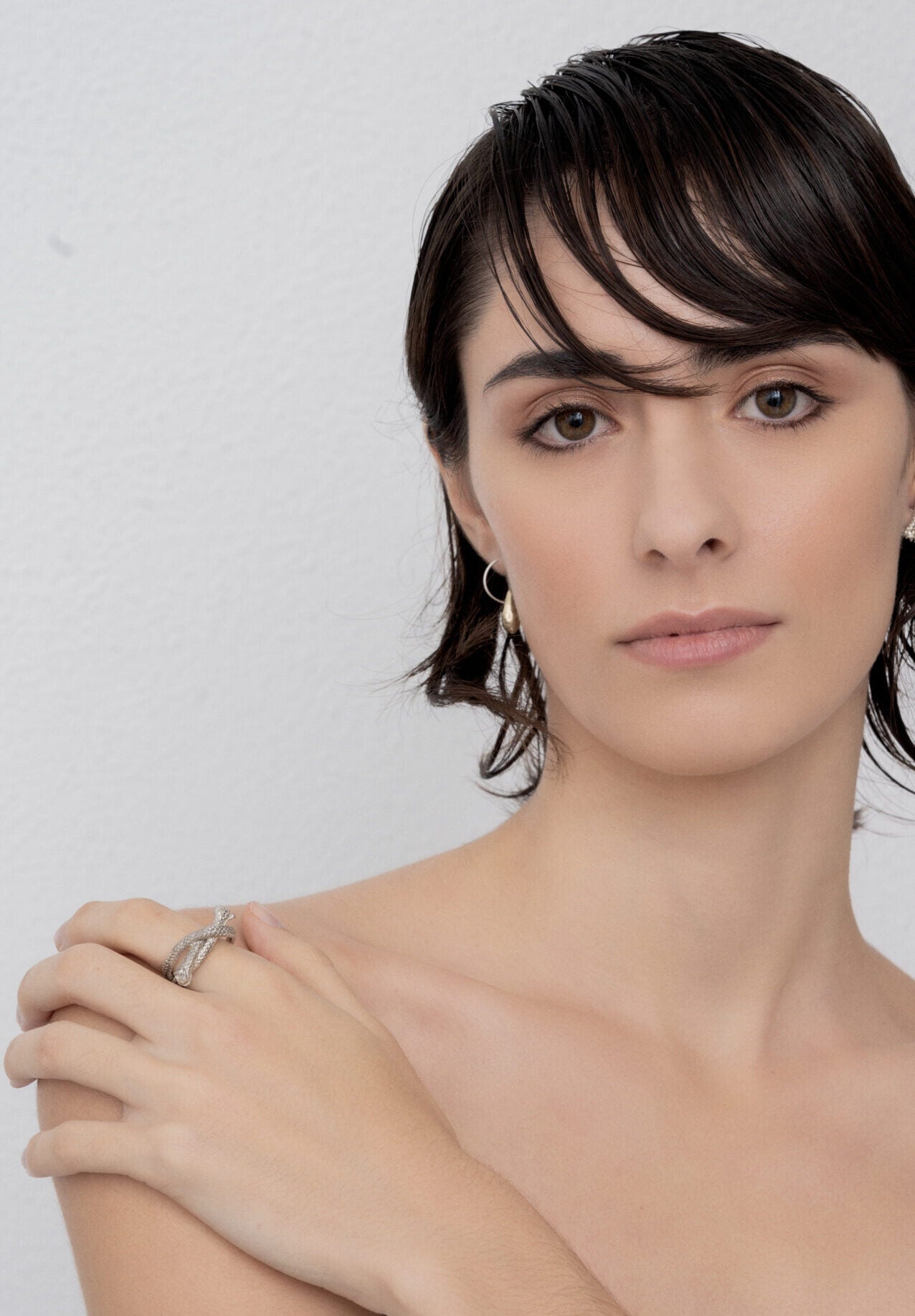 A person with short dark hair, wearing sterling silver hoop earrings and the Ballestrinque Knot - Clove Hitch Artisanal Nautical Ring, poses against a plain background, looking directly at the camera.