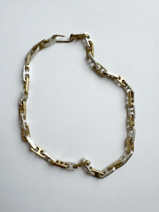 Gold and silver chain necklace on a light gray background by Angela Lago