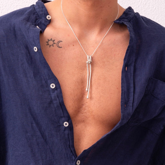 A person wearing an unbuttoned navy blue shirt with a sun and crescent moon tattoo on their chest and an Artisanal Made Ballestrinque Nautical Knot Pendant necklace.