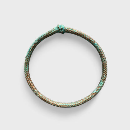 A circular, braided rope with intertwining green and brown hues that form a loop with a knot at the top, set against a plain white background—an exquisite *Artisanal Bronze Rope Bangle Inspired by Natural Nautical Oxidation*.