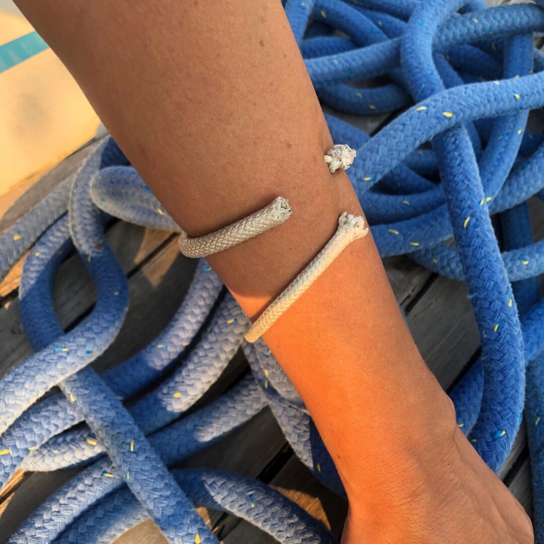 A rope is wrapped around a person's forearm, complemented by a Sterling Silver Thick Rope Cuff Bracelet Handmade, with additional blue rope coiled in the background on a wooden surface.