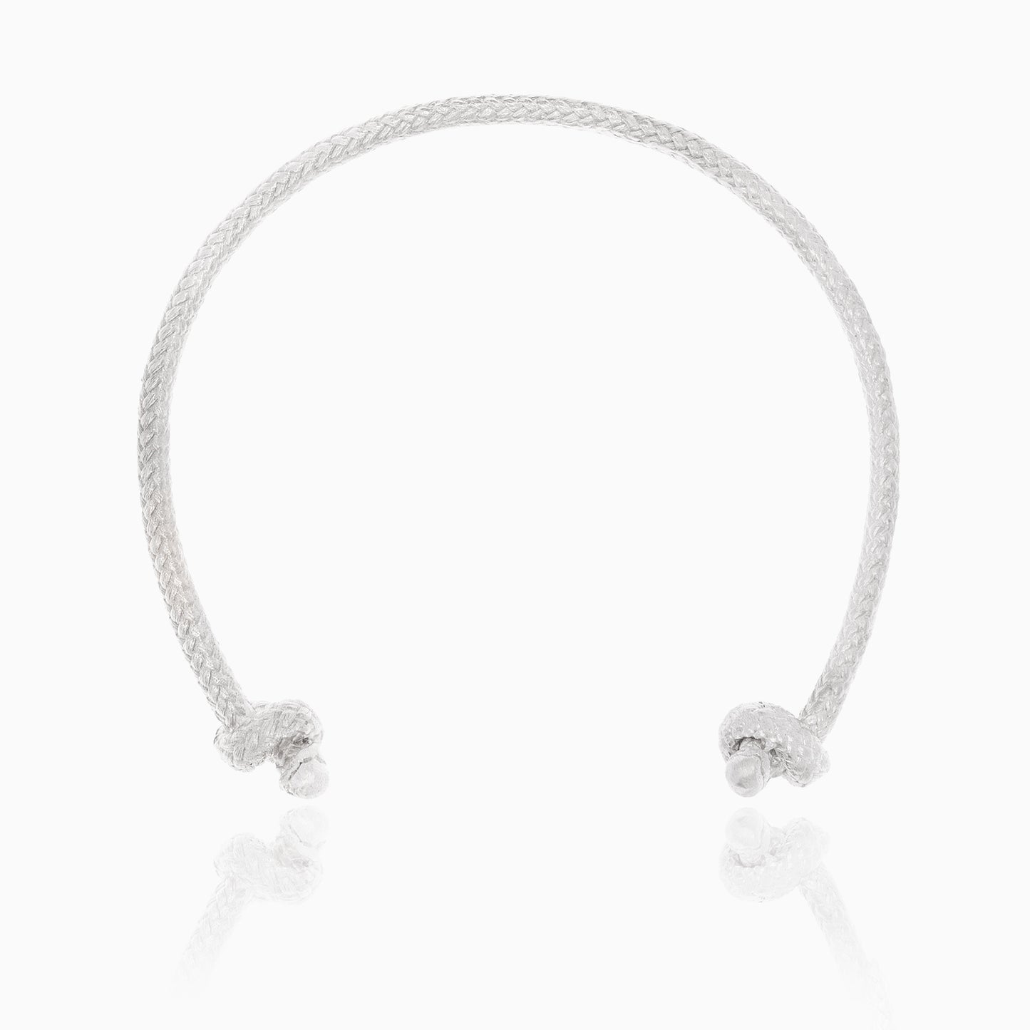 The Nautical Atlantic Bracelet Rope Cuff, crafted in sterling silver, features a braided design with smooth ends adorned by small round embellishments. This artisanal piece exudes a nautical touch and is showcased on a white background with a subtle reflection beneath the bracelet.