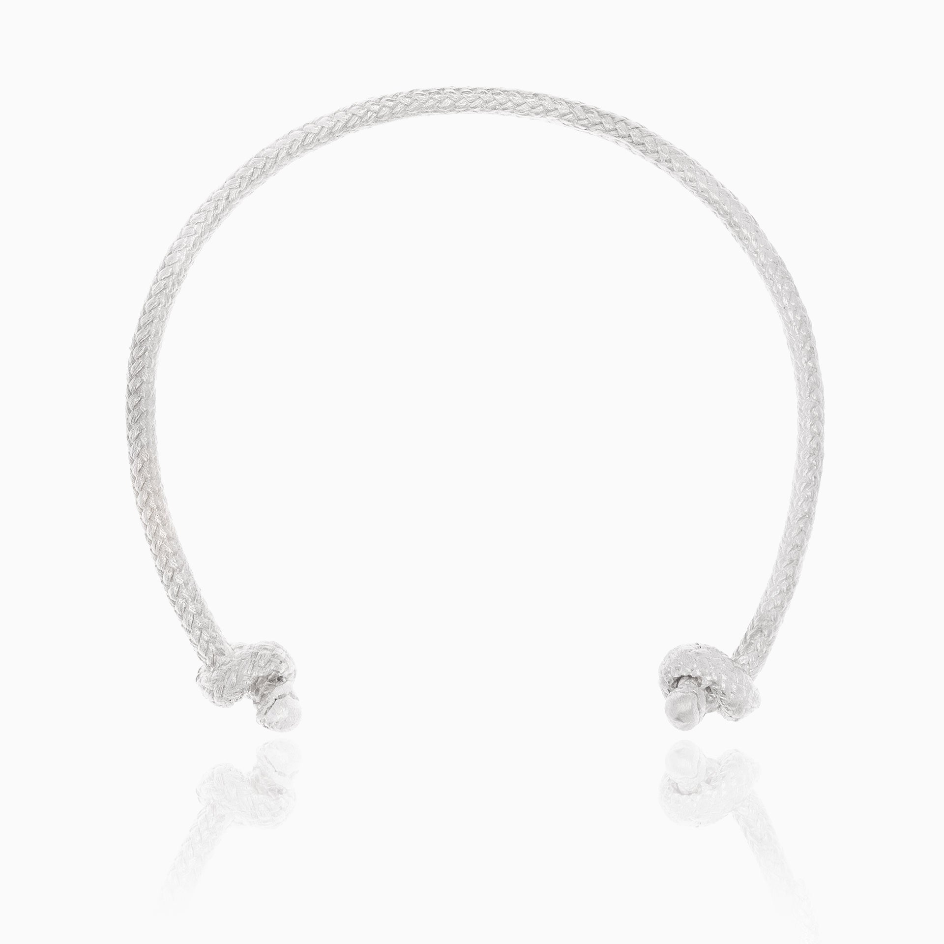 The Nautical Atlantic Bracelet Rope Cuff, crafted in sterling silver, features a braided design with smooth ends adorned by small round embellishments. This artisanal piece exudes a nautical touch and is showcased on a white background with a subtle reflection beneath the bracelet.