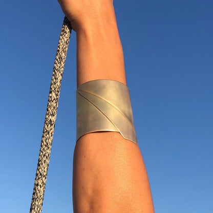 A person's arm wearing the wide Sea Wake bracelet, crafted from 100% Sterling Silver, is holding a braided rope against a clear blue sky.