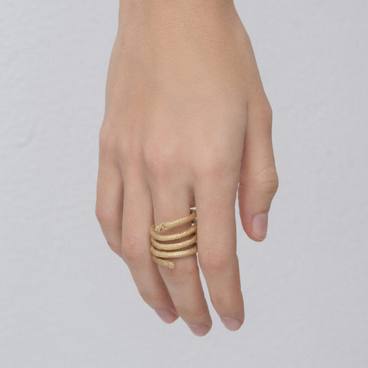 A hand adorned with the Curly Handcrafted Rope Ring III, a gold-plated brass (5 microns gold) masterpiece featuring an intricate, multi-band design that elegantly wraps around the finger. The plain, light-colored background accentuates the exquisite craftsmanship of Angela Lago's creation.