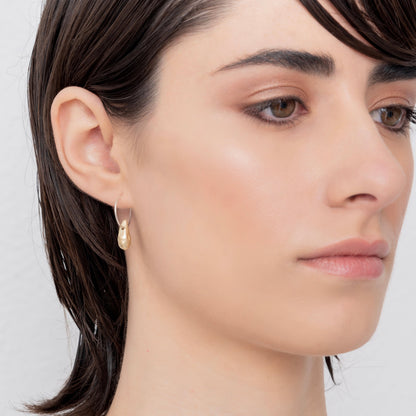 Close-up of a person with short, dark hair wearing Golden Drop Hoop Earrings Nautical Inspired, handmade by Angela Lago, looking slightly to the side with a neutral expression.