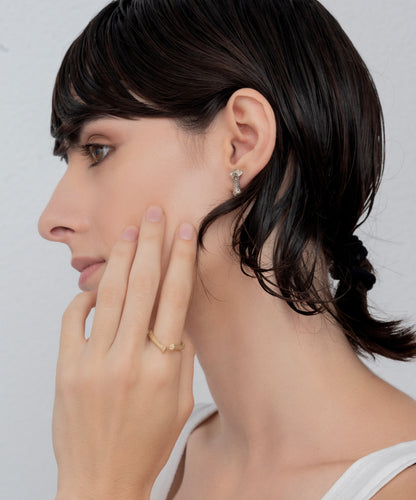 Side profile of a person with short, dark hair wearing a hoop earring with a handmade dangling charm and touching their face, showcasing the Golden open rope ring.