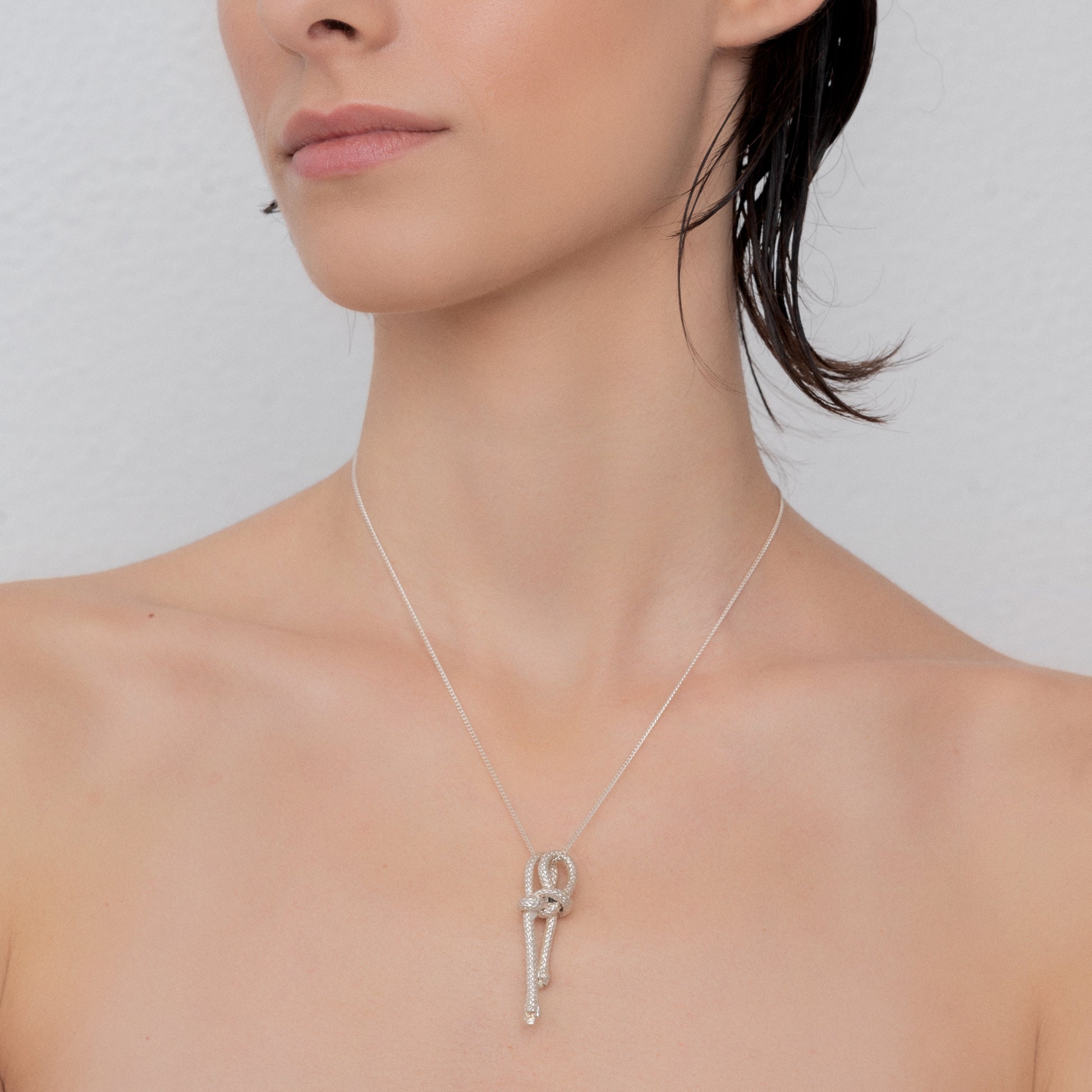 A woman with short, wet hair wears a sterling silver chain featuring a Ballestrinque Small Nautical Knot Pendant, photographed from the shoulders up against a light gray background.