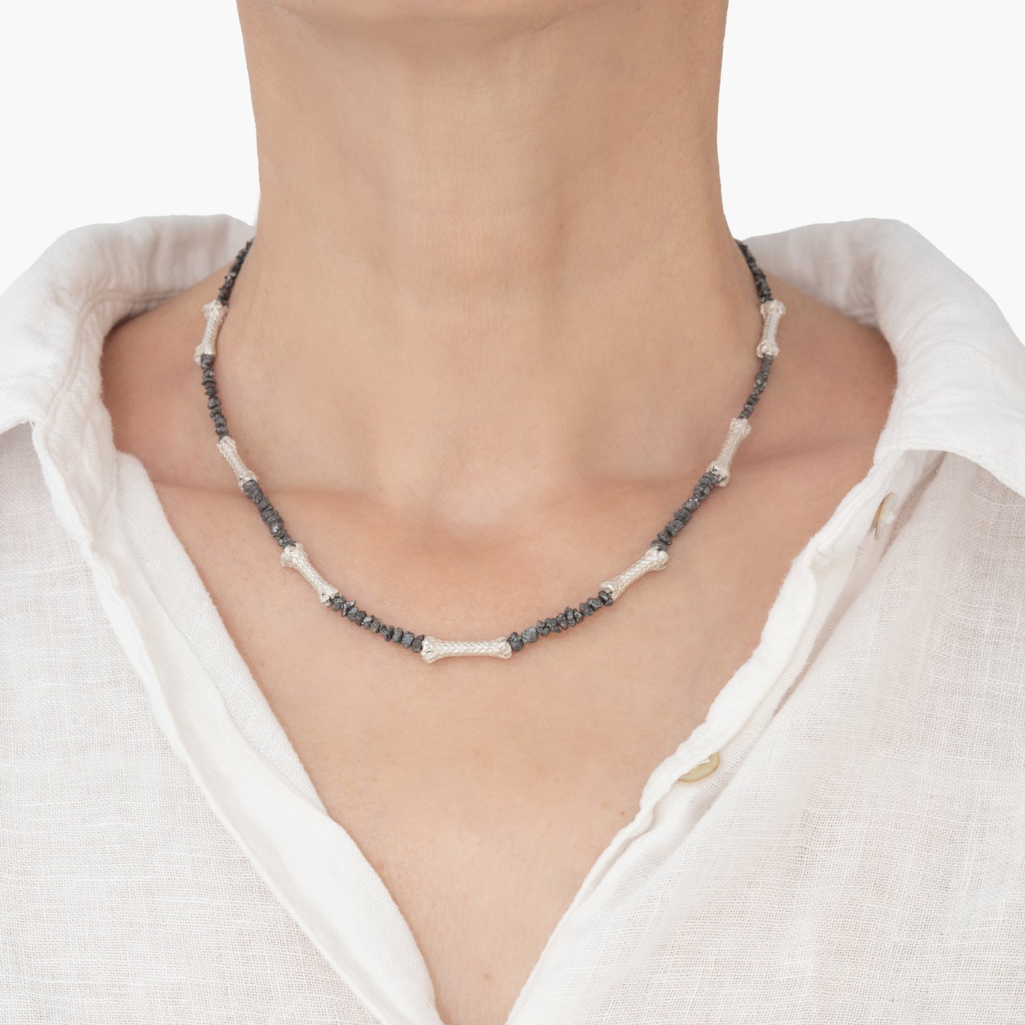 A person wearing a white shirt and a one-of-a-kind necklace featuring raw black diamonds and sterling silver ropes, elegantly handcrafted with artisanal precision.