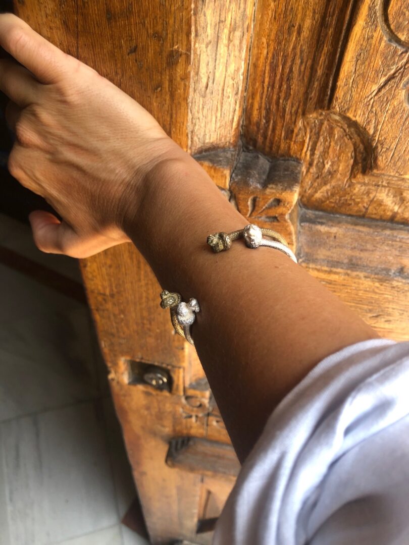 A hand wearing a Nautical Atlantic Bracelet Rope Cuff with animal-shaped charms reaches out to open a wooden door with intricate carvings.