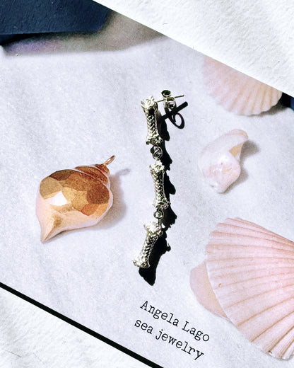 A Three Sterling Silver Ropes Nautical-Inspired Earring lies on a paper with the text "Angela Lago sea jewelry," surrounded by small seashells. This artisanal made piece complements the delicate beauty of the ocean.