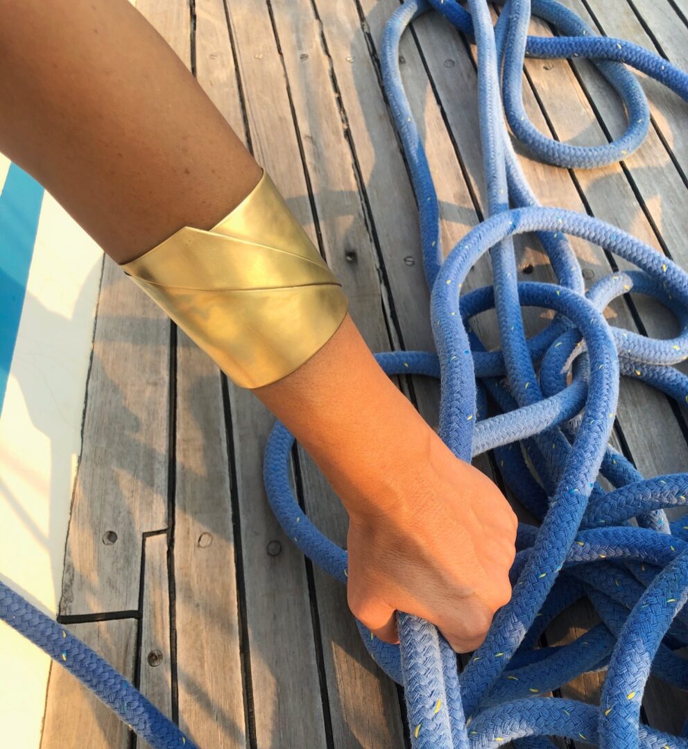 A person wearing a Sea Wake bracelet handmade by Angela Lago holds a blue rope on a wooden deck.