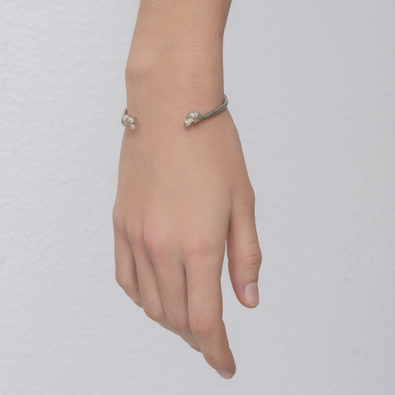 A close-up of a person's hand wearing the Nautical Atlantic Bracelet Rope Cuff with two small decorative ends. The background is a plain, light-colored wall.