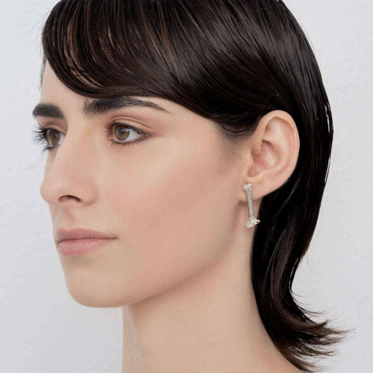 A person with short dark hair wearing an Earring Sterling silver rope M, crafted from 100% Sterling silver by Angela Lago.