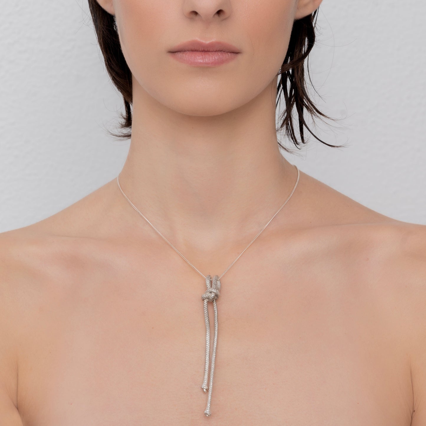 Close-up of a person wearing the Artisanal Made Ballestrinque Nautical Knot Pendant, crafted from sterling silver, against a plain white background. The necklace features two hanging strands.