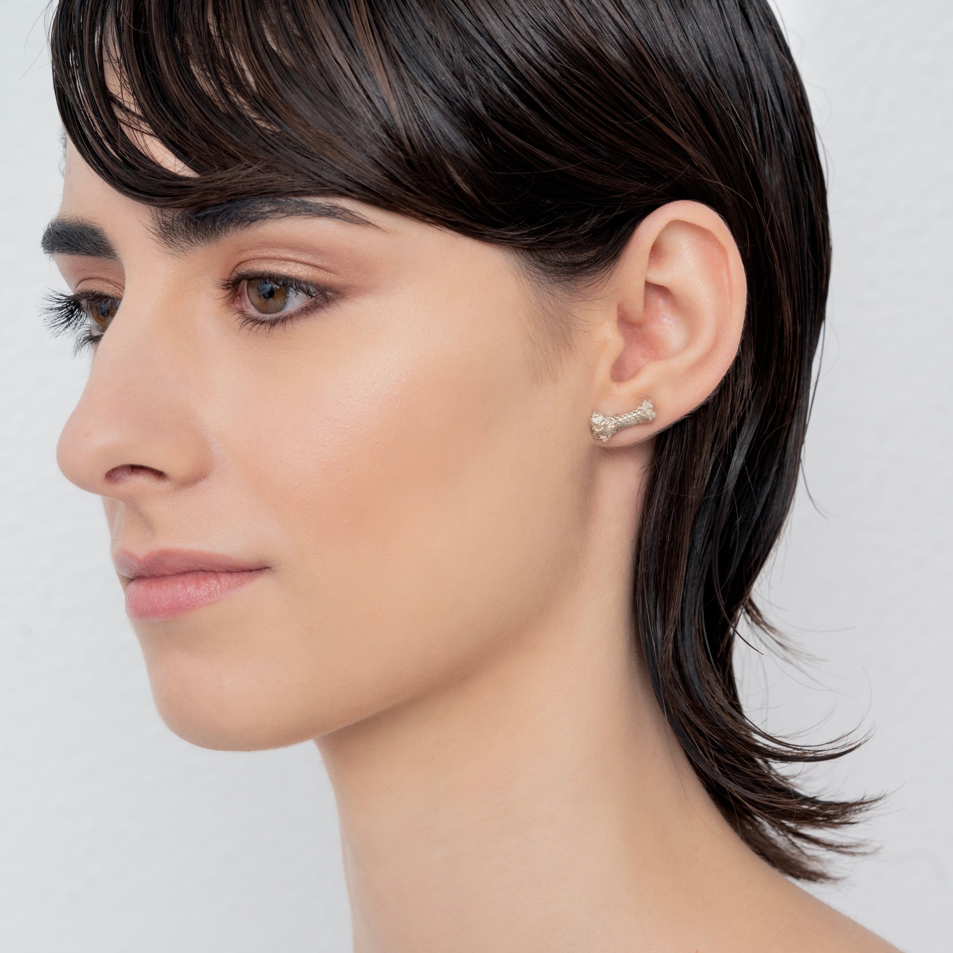 Side profile of a person with short, wet hair, wearing a small Sterling Silver Rope S Earring: Handmade Nautical Jewel on the left ear. The background is plain white.